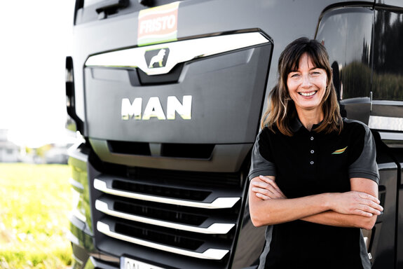 Ein neuer LKW, der für den FRISTO Getränkemarkt im Einsatz ist, mit dem überarbeiteten Unternehmenslogo auf der Front. Davor steht ein freundlicher Mitarbeiter in unserem Firmenpolo in den Unternehmensfarben.